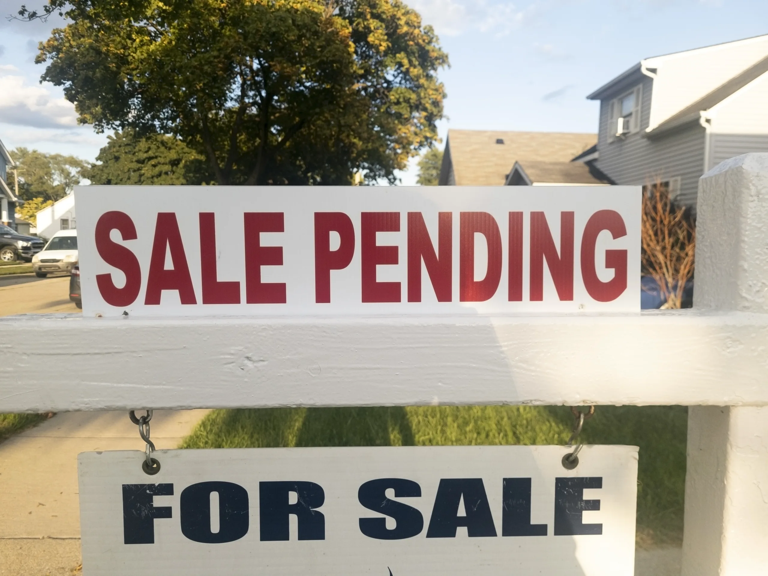 Sale pending sign above a for sale sign with the neighborhood behind it